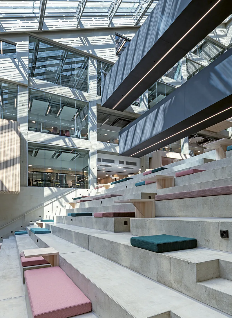 Wide concrete seating steps with pink and green cushions under EduCity's glass roof.