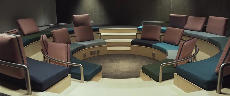 A small round amphitheatre with cushioned seats in rose and teal around a sunken centre.