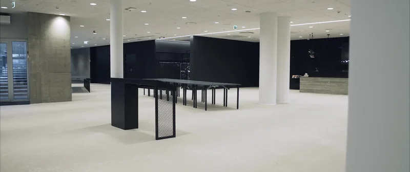 Joki's empty lobby: a light floor, white pillars, long black high tables and a light wood-look reception counter.